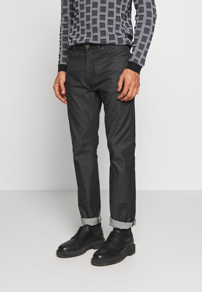 Mörkgrå denimbyxor med rak passform, uppvikta fållar och en slät yta, tillsammans med svarta snörskor i läder.