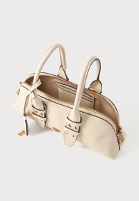 Kis krémszínű kézi táska arany cipzárral, két felgöngyölt fogantyúval, elülső csat részletekkel és nyitott tetejével, amely belső zsebet mutat.