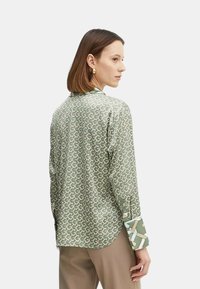 Camisa de manga larga verde con un patrón, de textura suave. Presenta puños con un patrón contrastante. Corte casual con cuello y dobladillo curvado.