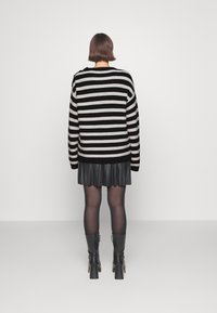 Czarny sweter w paski w kolorze kremowym o luźnym kroju, w połączeniu z czarną plisowaną spódnicą i czarnymi wysokimi butami na obcasie.