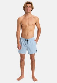 Light blue swim shorts with an elastic waistband, drawstring closure, and a small logo patch on the hem. Material appears textured.