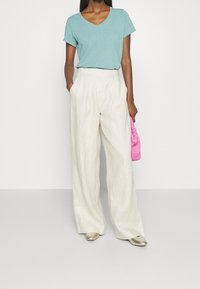 Světlé lněné kalhoty širokého střihu spárované s azurovým tričkem s v-výstřihem. Doplňkem je růžová pletená kabelka a metalické boty.