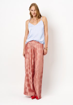 Lichtblauwe satijnen camisole met dunne spaghettibandjes, gecombineerd met roze geplooide broek met wijde pijpen en een golvende textuur, en rode schoenen met spitse neuzen.