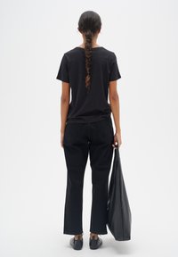 Tricou negru din bumbac cu mâneci scurte, asociat cu pantaloni negri din denim și pantofi negri lejeri. Ține în mână o geantă mare neagră.