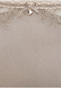 Beiger Stoff mit glatter Textur, verziert mit aufwendigen Spitzendetails am oberen Rand, einem kleinen Bogen und einem dekorativen Anhänger in der Mitte.