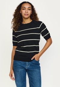 Črni pulover s kratkimi rokavi z belimi horizontale črtami, okrogel izrez in rebrast rob. Združen z modrimi džins hlačami.