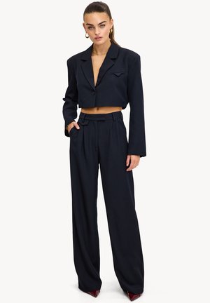 Blazer negro recortado con un solo botón y bolsillo, combinado con pantalones negros de pernera ancha de tiro alto, con cintura con cinturón.