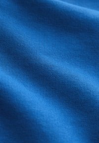 Niebieska dzianina o delikatnej prążkowanej fakturze i subtelnych fałdach tworzących miękkie cienie.