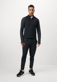 Sort atletisk pullover med kvart lynlås, teksturerede ærmer og matchende tætsiddende bukser. Har sidelommer og sorte sneakers.