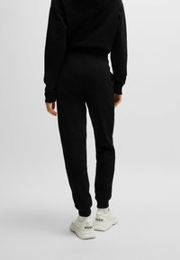 Zwarte joggers van zacht materiaal, met geribbelde boorden en een hoge tailleband, gecombineerd met witte sneakers met het label "HUGO."