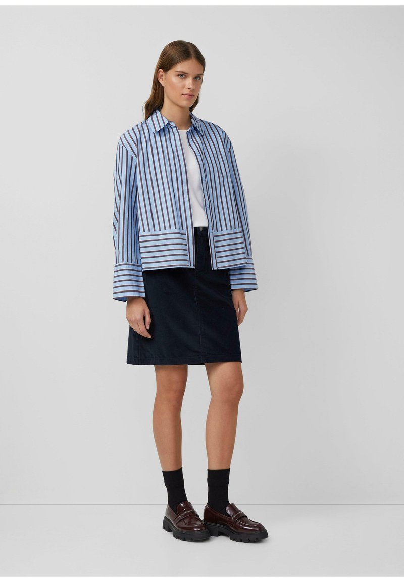 Gestreepte blauwe en witte jas met een kraag, gecombineerd met een marineblauwe rok. Model draagt donkere sokken en bruine schoenen met een stevige zool.