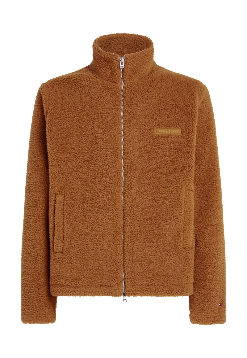 Giacca in pile marrone con colletto alto, chiusura frontale con zip, due tasche laterali e un piccolo dettaglio del logo sul petto. Materiale morbido e testurizzato.