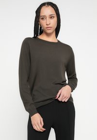 Rudas megztinis su ilgomis rankovėmis, apvalia apykakle ir apsiūtais rankogaliais. Lengvos medžiagos, švelnios tekstūros, stilingai dėvimas laisvalaikiui su juodomis kelnėmis.