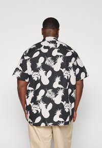 Zwarte shirt met witte ananas- en bladdessins, korte mouwen, losse pasvorm en een klassieke kraag. Geweven stof met een gladde afwerking.