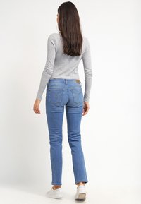 Blå denimjeans med slim fit, med en midjeres höjd, diskret sömnad på bakfickorna och en ljus tvätt. Matchas med en grå långärmad topp.