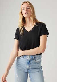 Tricou negru cu decolteu în V, fabricat dintr-un material moale, asortat cu blugi deschiși la culoare cu talie înaltă, cu accente uzate și o siluetă ajustată.