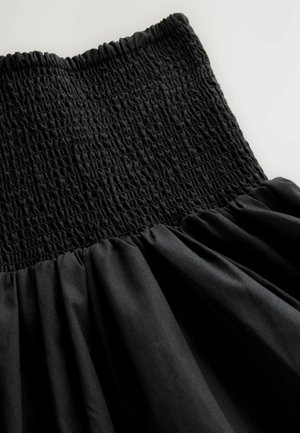 Sort kjole med en smocket overdel og et flydende, rynket skørt. Stoffet har en glat tekstur med en let glans.