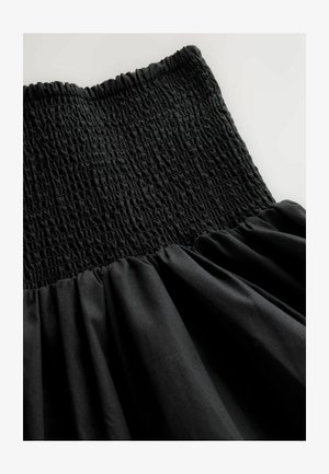 Sort kjole med en smocket overdel og et flydende, rynket skørt. Stoffet har en glat tekstur med en let glans.