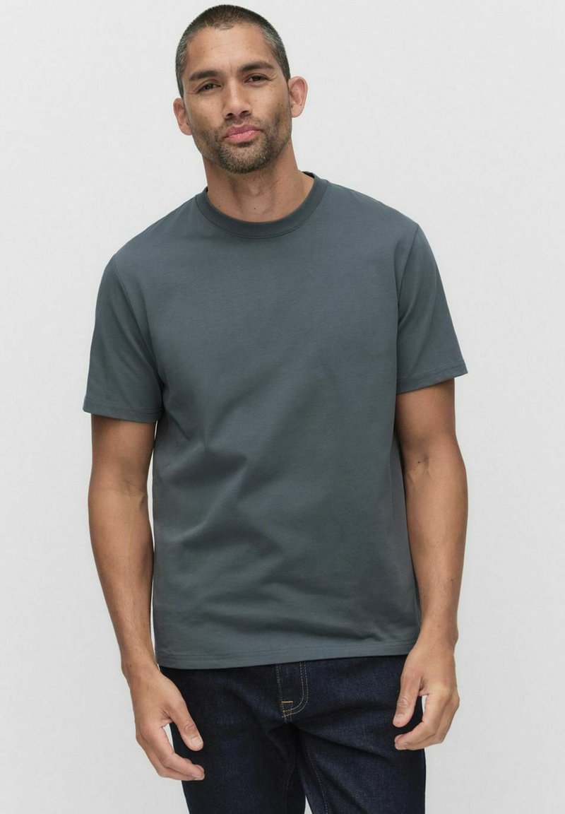 Mörkgrå kortärmad t-shirt, rund hals, gjord av bomull. Bärs med mörka jeans. Slät textur, kroppsnära passform. Enkel, utan mönster eller logotyper.