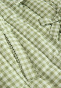 Gepolsteter Stoff in Grün-Weiß mit kariertem Muster und weicher Textur, mit abgesteppten Fächern und einer Schleifendetail.