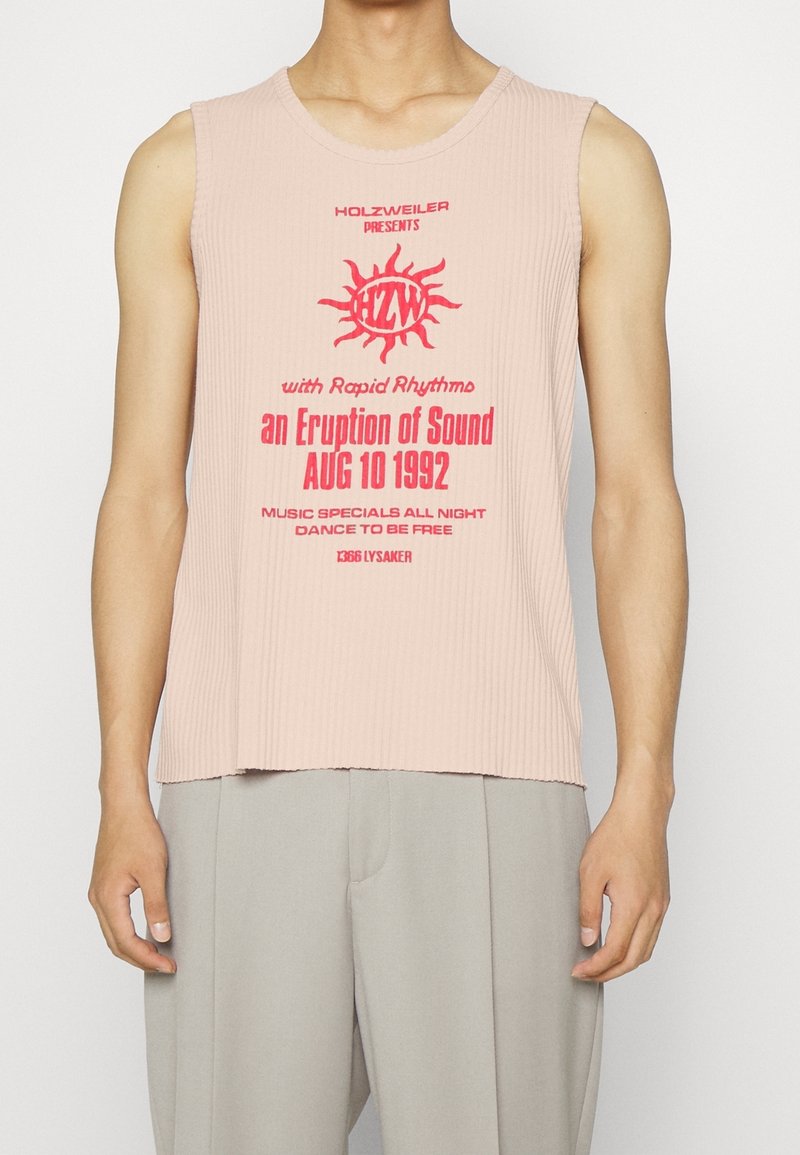Sleeveless ribbed light pink top with red print text about a 1992 music event, worn by a person with arms relaxed at sides.