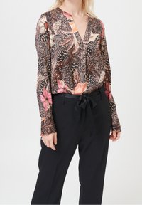 Blouse à manches longues avec un fond noir orné de motifs floraux et géométriques colorés, associée à un pantalon noir taille haute avec une ceinture nouée.