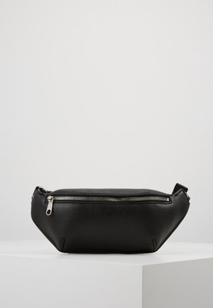 Černá texturovaná kožená ledvinka se stříbrným zipem a nastavitelným popruhem, vystavená na bílém podstavci na světle šedém pozadí.