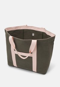 Torba na ramię w kolorze oliwkowej zieleni z różowymi płóciennymi rączkami, prostokątnym kształtem, otwartą górą i prostym wnętrzem. Zawiera małą metkę z logo wewnątrz.