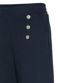 Ceinture de pantalon bleu marine avec élastique et trois boutons-pression argentés alignés verticalement près de la poche avant.