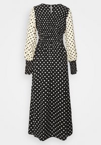 Svart och vit prickig långärmad midiklänning med kontrasterande ärmar, smockad midja och manschettärmar.