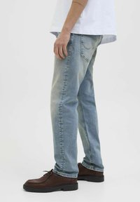 Jeans en denim bleu clair avec une coupe droite, design standard à cinq poches et un léger délavage, associés à des chaussures à lacets marron.