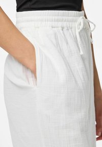 Pantalons blancs légers avec une taille élastique et un cordon de serrage. Comprend des poches latérales et un tissu doux et texturé.
