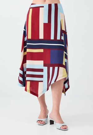 Jupe avec un ourlet asymétrique dans un motif géométrique rouge, bleu, jaune et blanc portée avec des talons ouverts bleu clair.