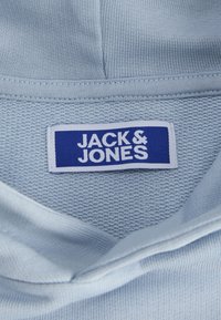 Svetlo modra tkanina z teksturiranim tkanjem, na kateri je prišit bel napis, ki prikazuje ime blagovne znamke "JACK & JONES" v modrem besedilu.
