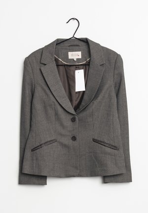 Blazer gris pour femme sur mesure avec deux boutons, col à revers cranté et poches fendues à l'avant, suspendu sur un cintre noir avec une étiquette de prix blanche.