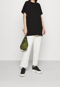 Černé žebrované oversized tričko, bílé široké kalhoty, černé chunky tenisky a zelený batoh se stahovací šňůrkou. Jednoduchý a minimalistický design oblečení.