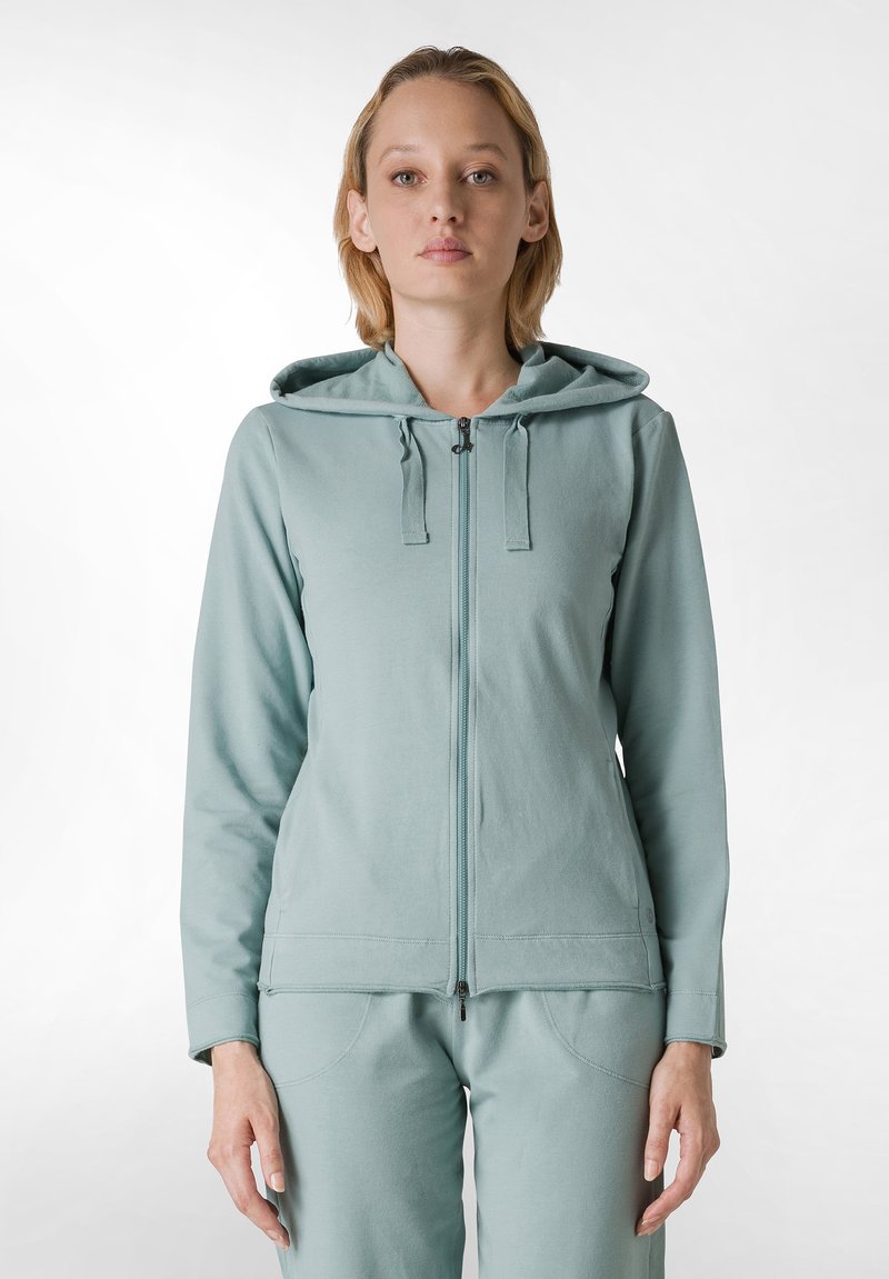 Felpa azzurra chiara con zip, cappuccio, tasche frontali e dettagli con cordino. Tessuto morbido con una texture liscia.