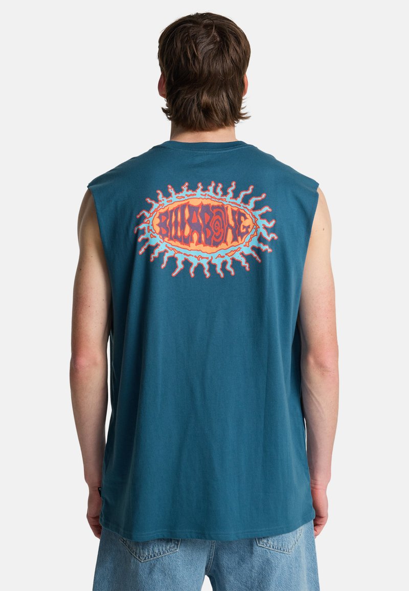 Mann trägt ein ärmelloses türkisfarbenes Hemd mit orange-rot gestyltem Sonnenlogo und Schriftzug auf dem oberen Rücken, kombiniert mit hellblauen Jeansshorts.