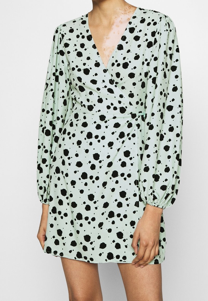 Robe courte vert menthe avec motif éclaboussé noir, décolleté en V, manches longues bouffantes et design portefeuille, présentant une texture lisse.