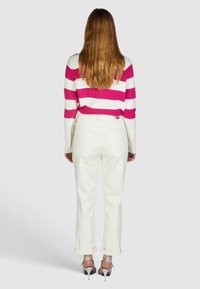 Pull rayé rose et blanc associé à un jean blanc taille haute et des sandales argentées à talons. Étiquette visible sur le jean ; coupe décontractée.