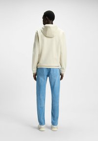 Cremefarvet hætte sweatshirt med en glat tekstur, parret med lyseblå jeans med baglommer og lige ben.