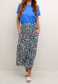 Blauw T-shirt gecombineerd met een lange bloemenrok, voorzien van witte en lichtblauwe bloemen op een marineblauwe achtergrond, met zakken en geplooide textuur.