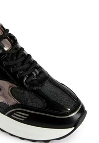 Sneaker nera con tomaia in pelle texturizzata, dettagli in rete e suola bianca spessa. Comprende lacci neri e accenti metallici.