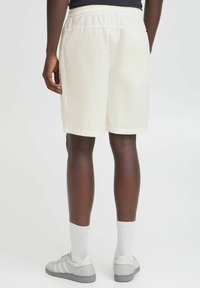 Lys beige shorts med elastisk talje, der når midt på låret, parret med grå sneakers og hvide sokker. Glat stof tekstur.