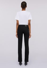 Černé džíny s rovnými nohavicemi, vybavené dvěma zadními kapsami, koženým nášivkem na pase a hladkým povrchem.