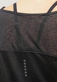 Černý sportovní top s průsvitným designem, s horizontálními pruhy, kulatým výstřihem a vzorovanými akcenty u spodní části.