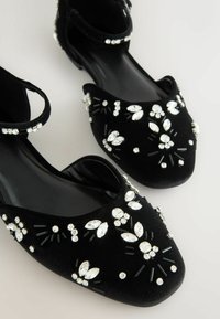 Czarne aksamitne baleriny z kryształowymi zdobieniami i subtelnie czarnymi akcentami. Posiadają okrągły czubek i design z paskiem w kostce.