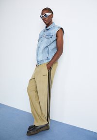 Denimvest med frynser, beige træningsbukser med sorte striber, og sorte platform sko. Modellen har hvide oversized solbriller på.
