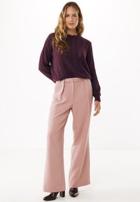 Maglione in maglia viola scuro con design a punto aperto, abbinato a pantaloni a gamba larga rosa chiaro a vita alta e scarpe con tacco quadrato marrone scuro.