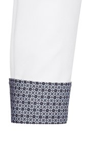 Manschetta di camicia bianca con una banda a motivo blu scuro caratterizzata da design geometrici in azzurro e bianco. Texture del tessuto liscia.